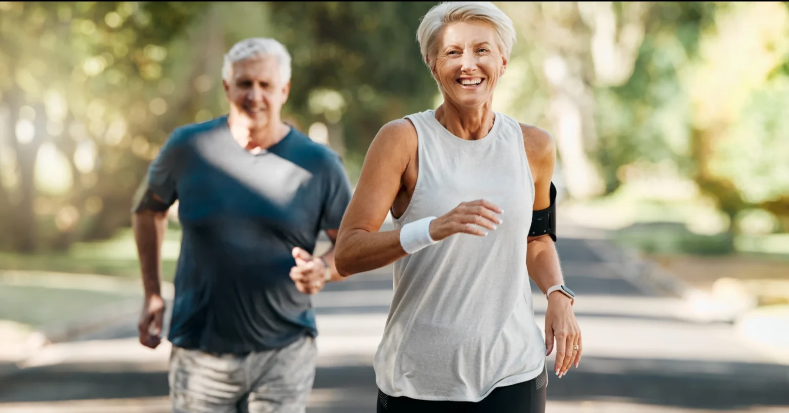 happy senior couple jogging through park