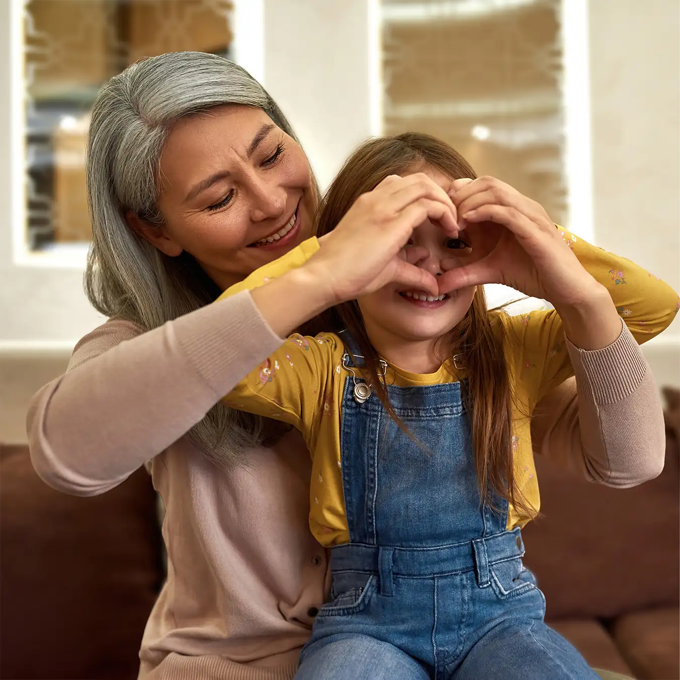playful grandmother and child making heart shape with their hands around eyes