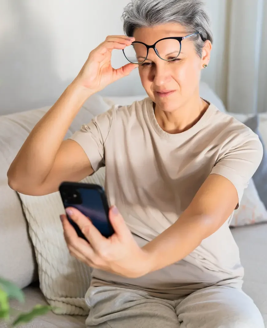 woman holding her phone away and squinting to see it