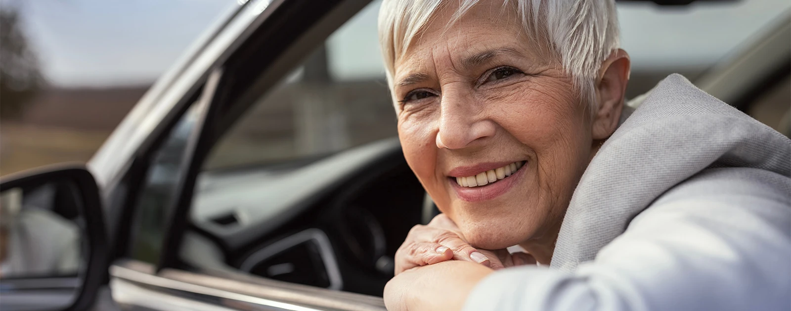 smiling senior woman in driver's seat looking out the car window
